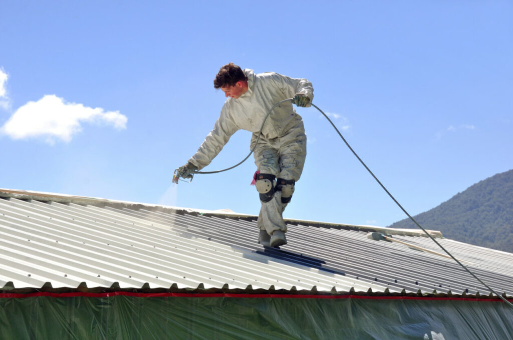 worker painting metal roof on home