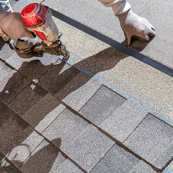 Roofer installing standard asphalt shingles on a residential roof, using staple gun to secure. 